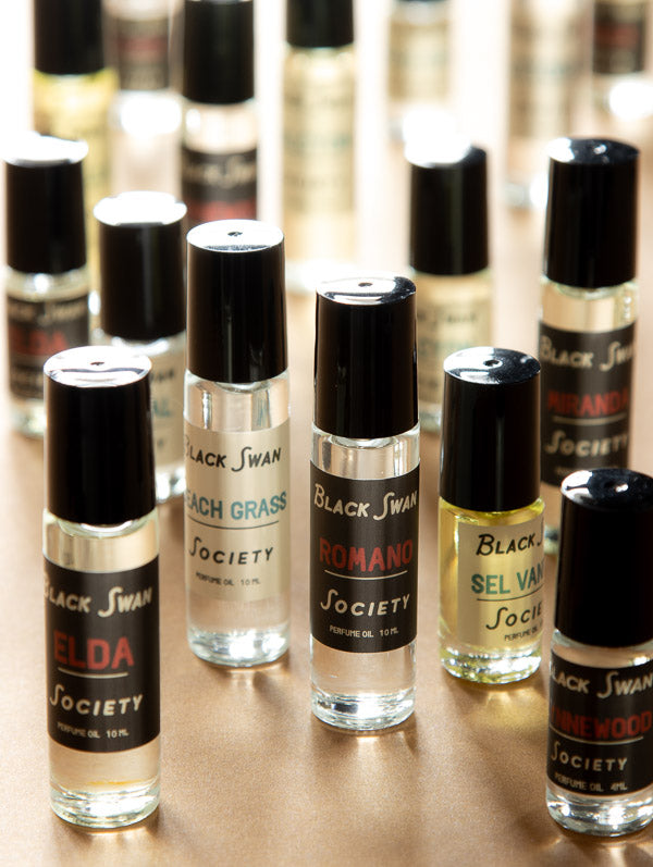 Collection of Black Swan Society perfume bottles on a reflective surface with blurred background