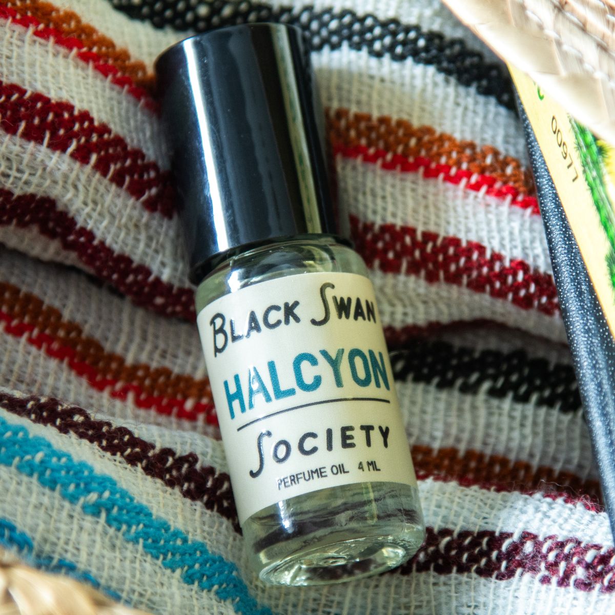 Perfume Oil Rollerball bottle with the label Black Swan Society Halcyon 4ml against a striped beach towel